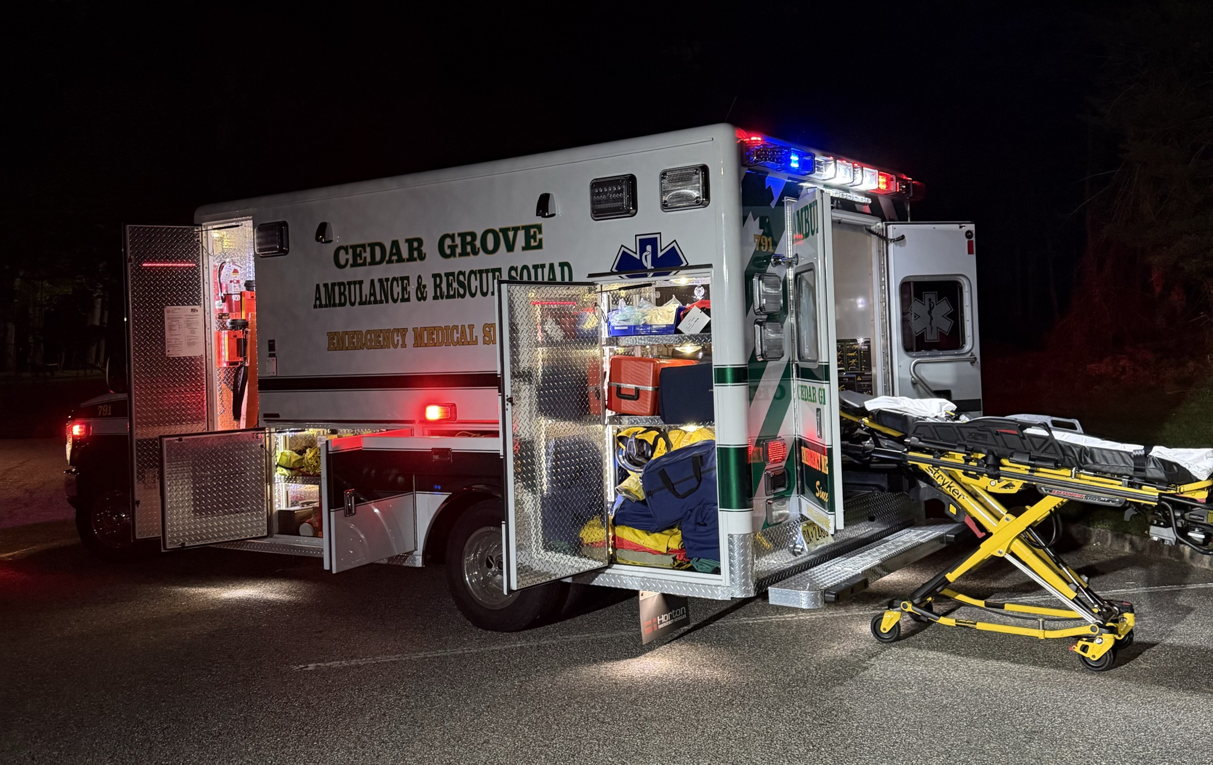 Cedar Grove ambulance with open compartments and a stretcher staged beside it at night