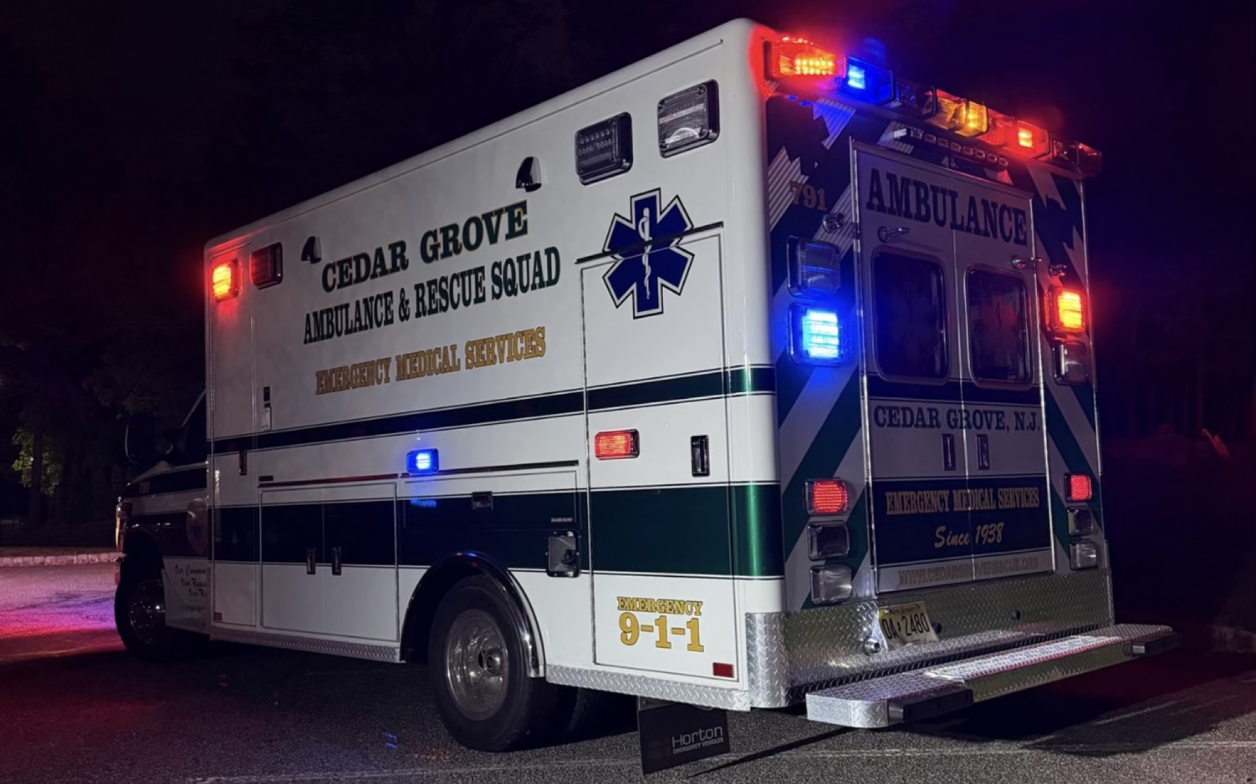Rear and side of a Cedar Grove ambulance with emergency lights on at night